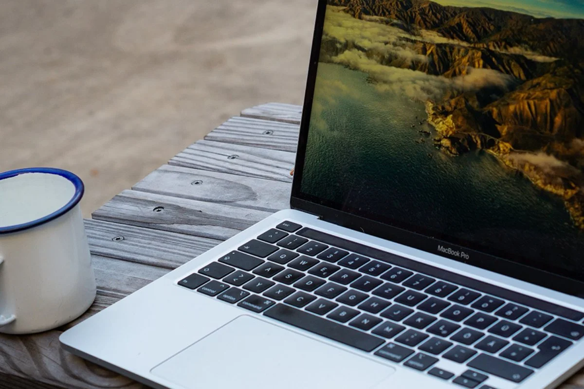 Aufgeklappter Laptop und Emaillebecher auf einem Holztisch im Innenhof des Hafven in Hannover