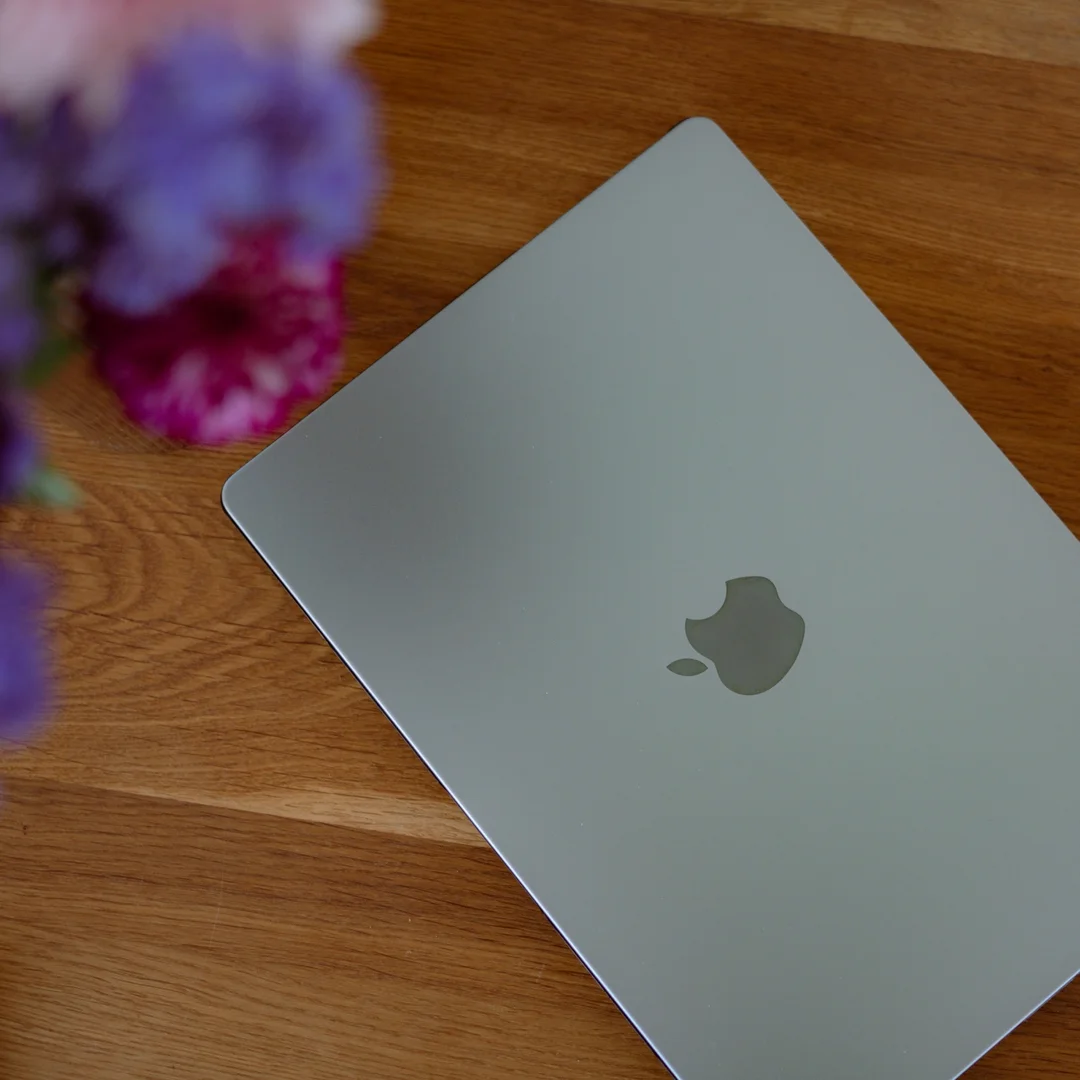 Ein geschlossenes MacBook auf einem Holztisch, daneben ein Strauß Blumen