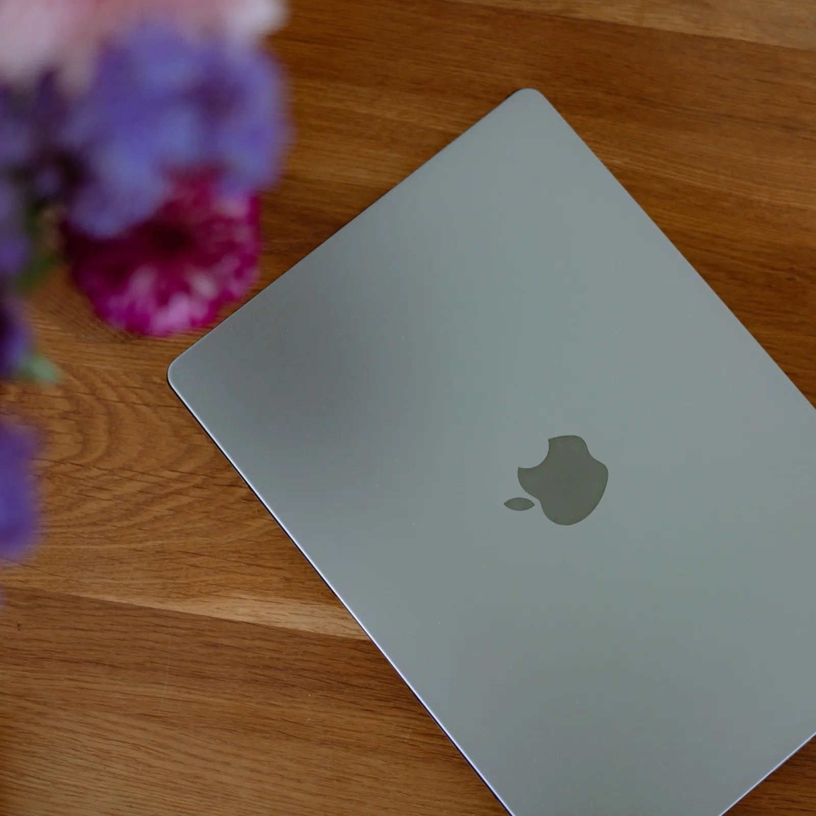 Ein geschlossenes MacBook auf einem Holztisch, daneben ein Strauß Blumen