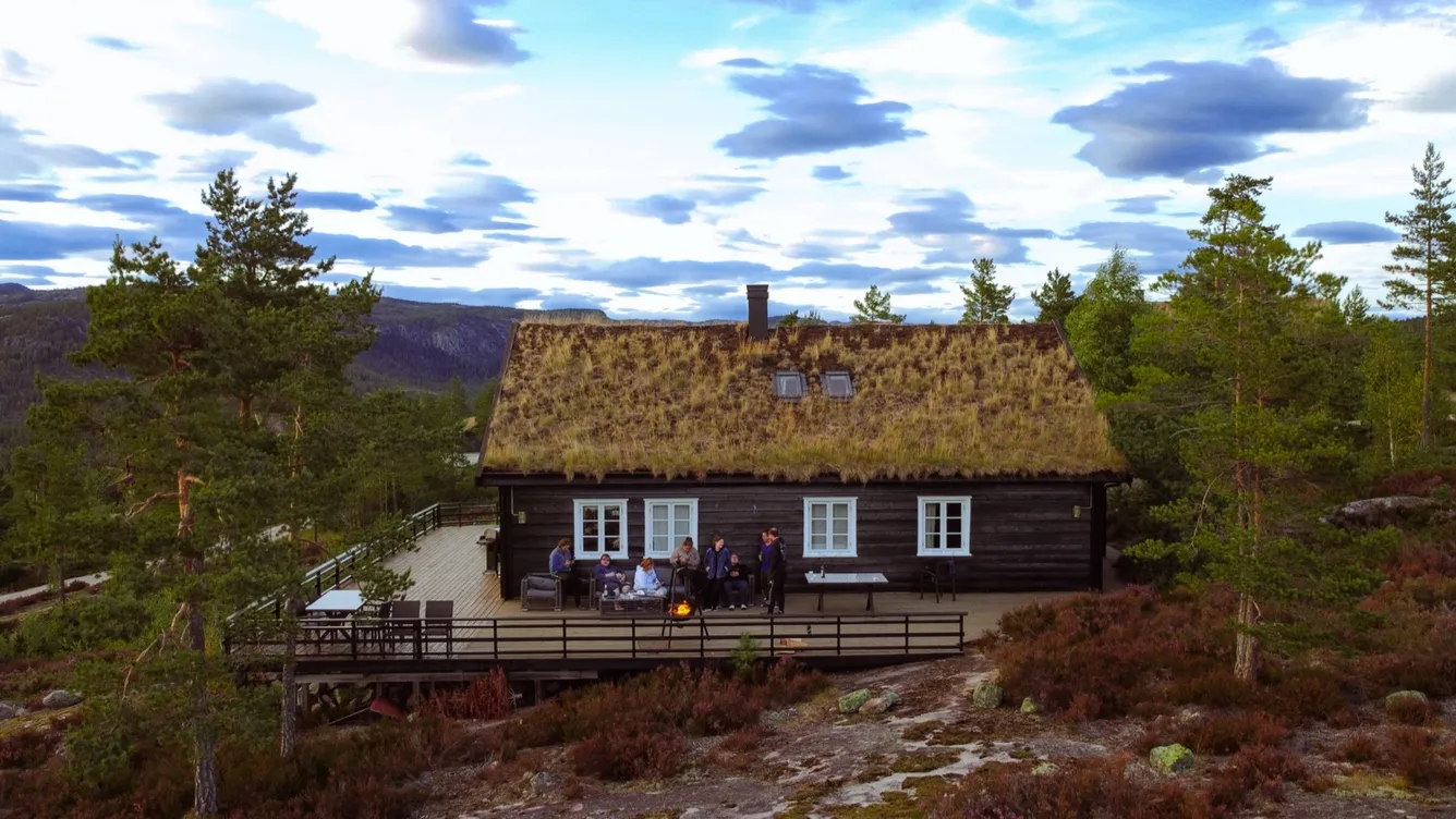 Hütte mit Grasdach in den Bergen, davor sitzen Leute auf der Terrasse