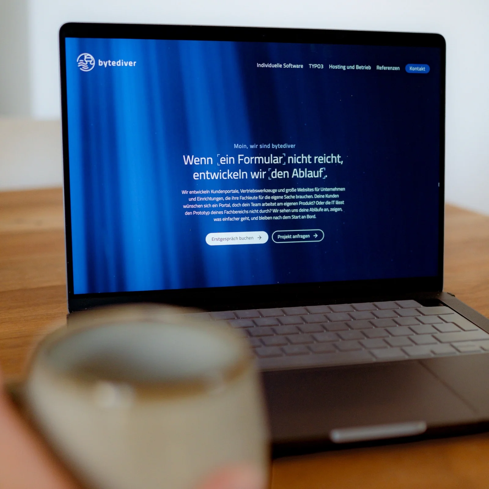 Ein Laptop auf dem Tisch zeigt die Startseite von bytediver, daneben eine Tasse