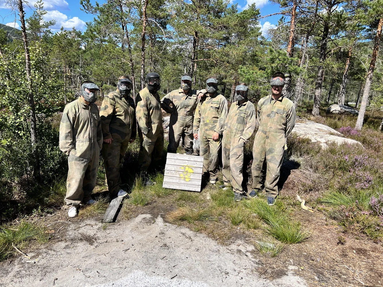 Die Crew in Overalls und Masken vor dem Paintball-Feld